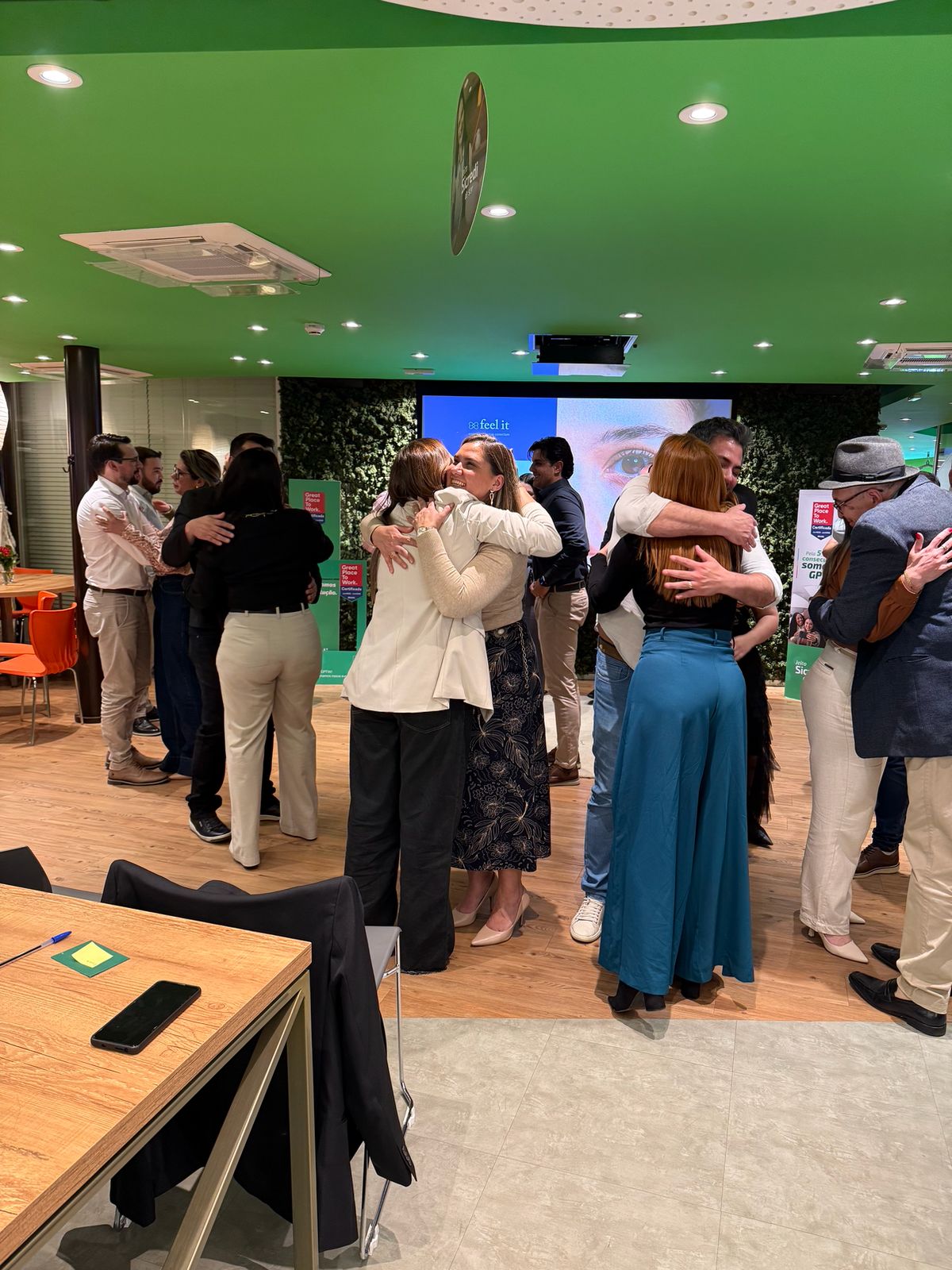 Participantes se abraçando diante do telão com o logo da Feel It durante uma degustação biográfica